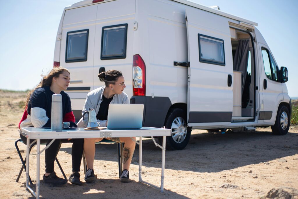 Young couple outdoors in Portugal, working on a laptop by their camper van.