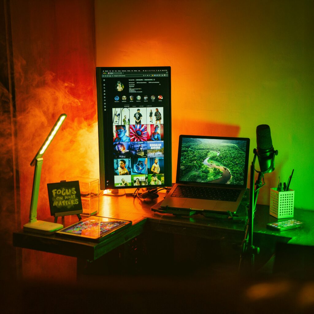 A vibrant home office space with a vertical monitor, laptop, and creative lighting.